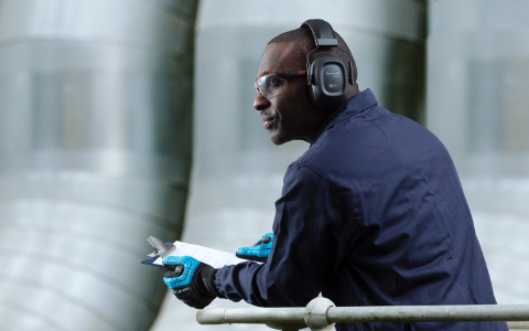 A worker wearing Honeywell protective earmuffs peers out over a balcony.