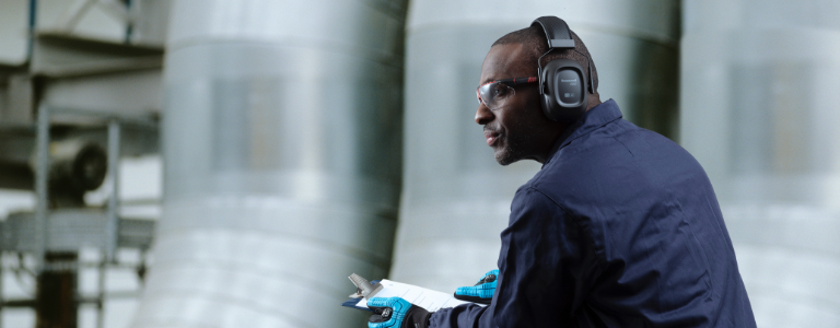 A worker wearing Honeywell protective earmuffs peers out over a balcony.