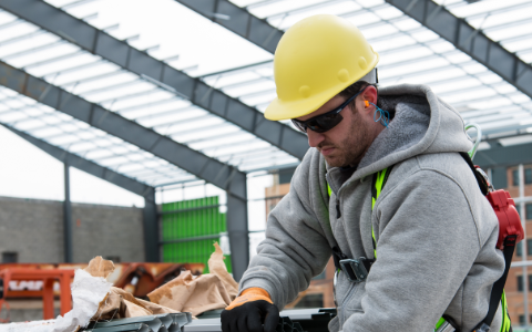 A worker wearing Honeywell Uvex safety glasses, earplugs, gloves, a hardhat and safety gloves lifts jobsite materials.