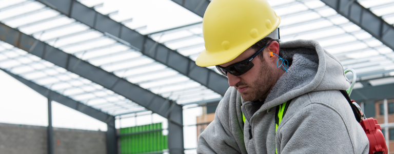 A worker wearing Honeywell Uvex safety glasses, earplugs, gloves, a hardhat and safety gloves lifts jobsite materials.