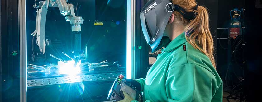 A welder in wearing a RADNOR welding helmets made by 3M Speedglas, controls an automated welding process