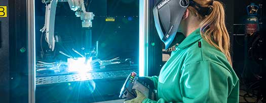 A welder is working a robotic welding arm.