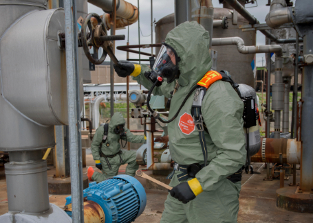 Worker is completely covered by DuPont protective clothing as he works outside next to machines, tanks and gears.