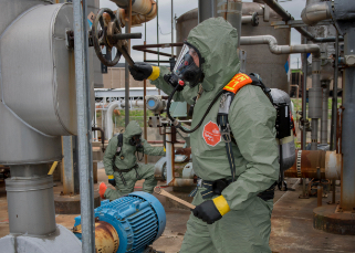 Worker is completely covered by DuPont protective clothing as he works outside next to machines, tanks and gears.