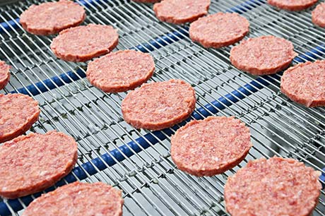 Multiple rows of meat patties on a food production line.