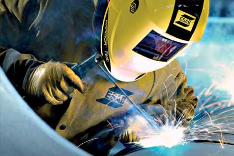 A welder performs a stick-welding application while wearing ESAB branded welding safety clothing and personal protective equipment (PPE), including a welding helmet, welding gloves and a welding jacket.